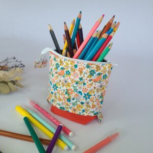 Trousse pot enfant à crayon rétractable. De couleur rose en bas et à motifs fleuri rose bleu turquoise, presence de quelques petits oiseaux dans les même couleurs.